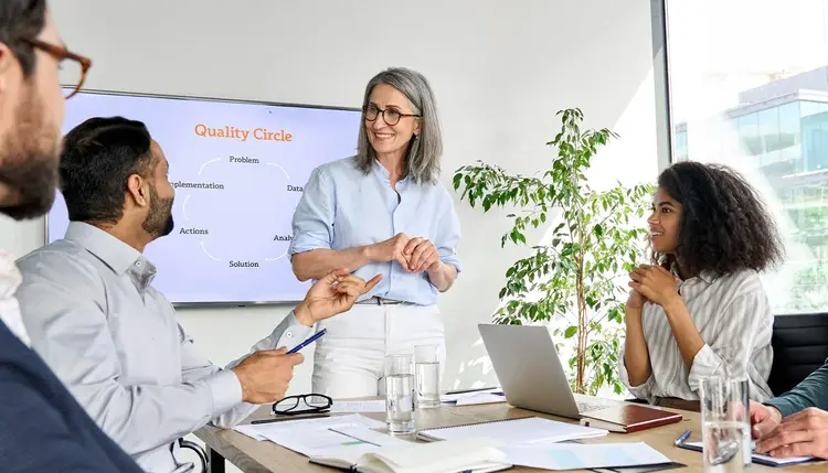 Quality circle in practice: Employees collaboratively analyze problems and develop improvement measures. Several employees sit together at a table discussing process improvements in a quality circle meeting.
